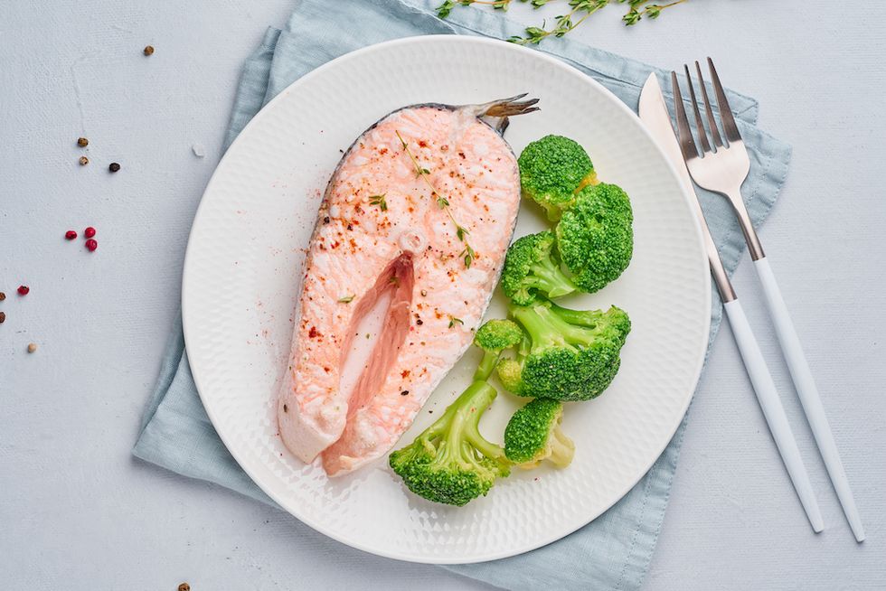 steam salmon, broccoli, paleo, keto or fodmap diet white plate on a blue table, top view