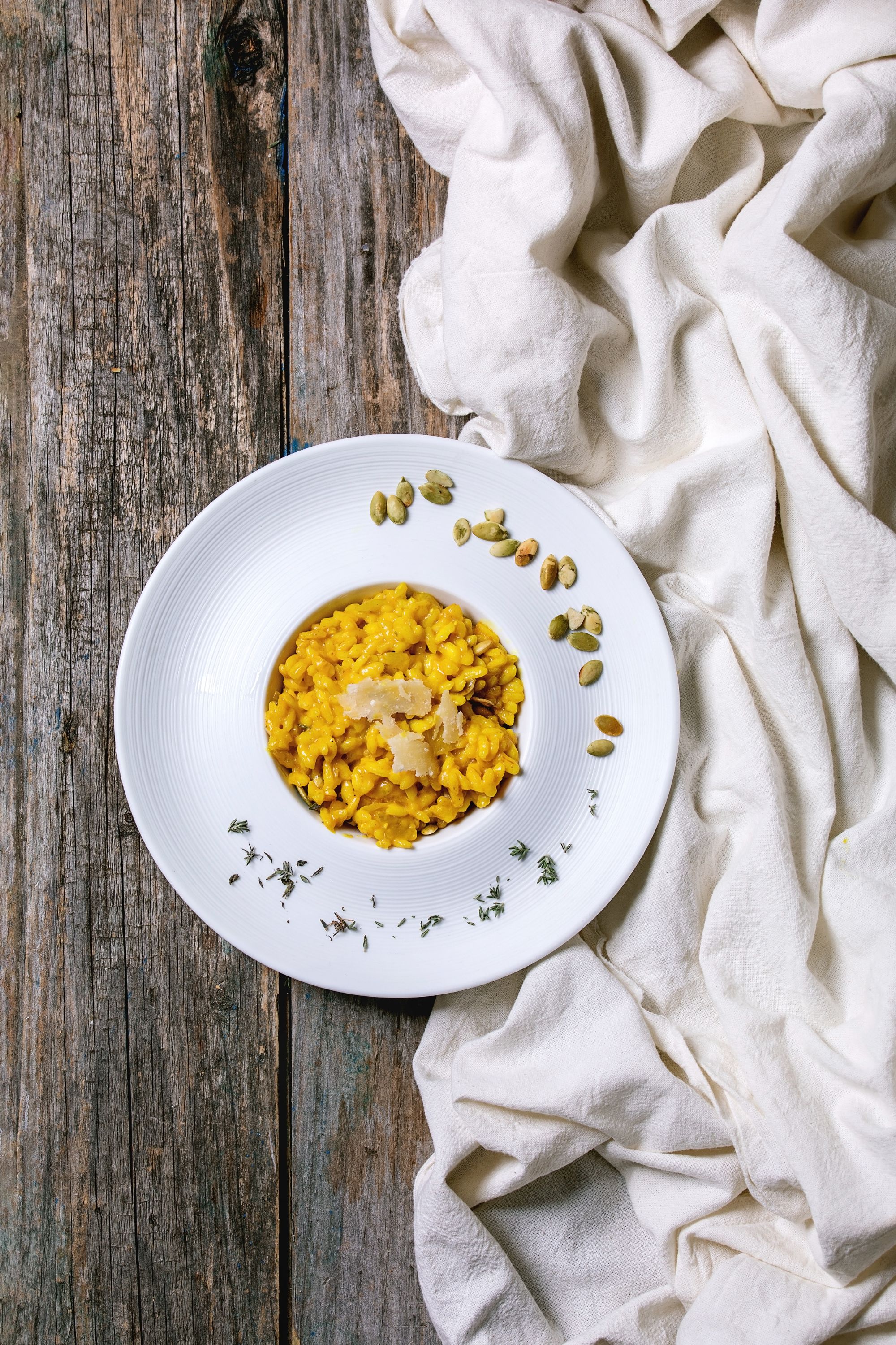 traditional vegetarian pumpkin risotto italian dish in ceramic plate over old wooden background with cloth, autumn leaves and ingredients above flat lay, space