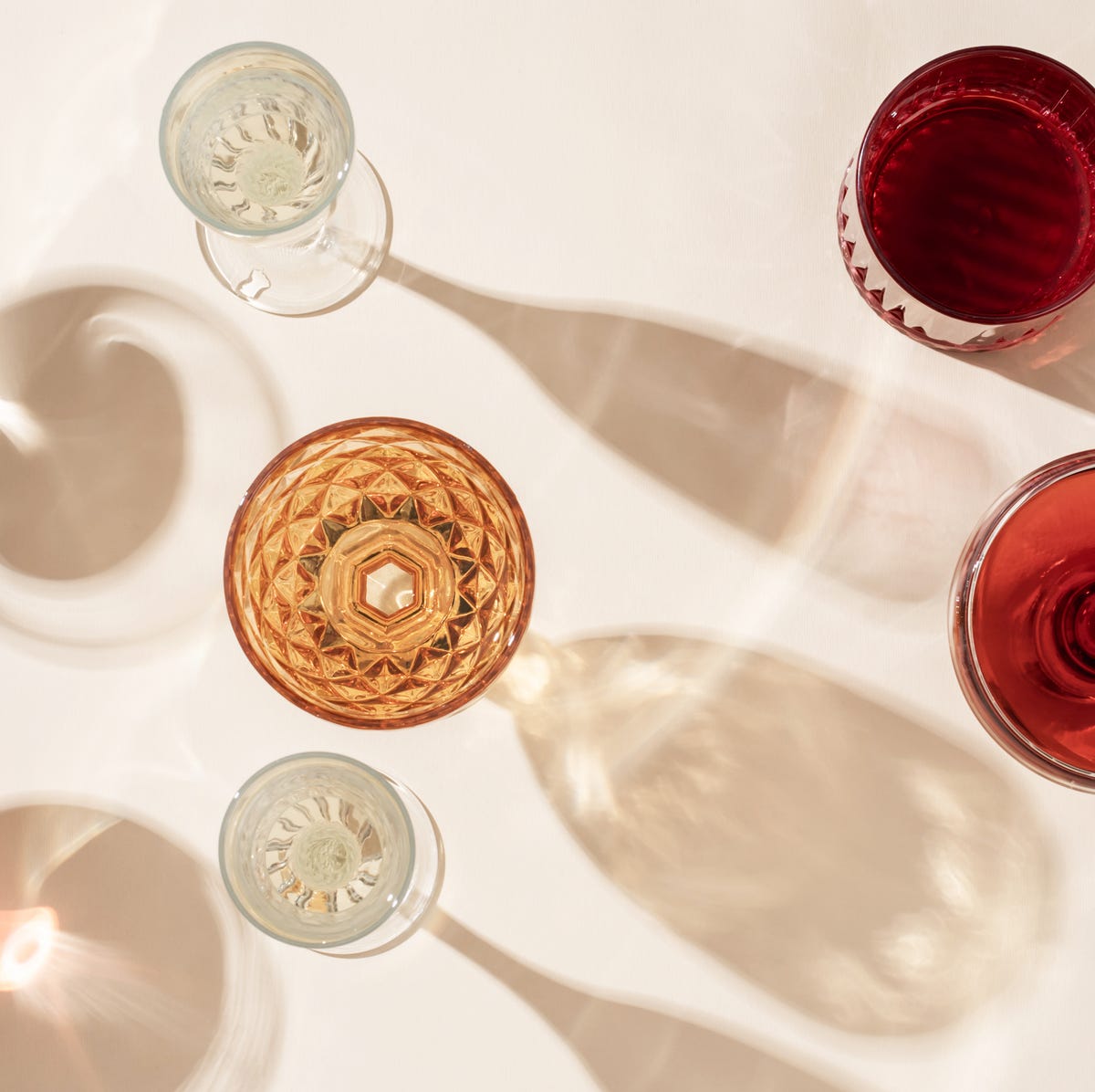 different glasses for wine, cocktails, drinks, long sun shadow on a light beige background the concept of wine tasting or summer vacation