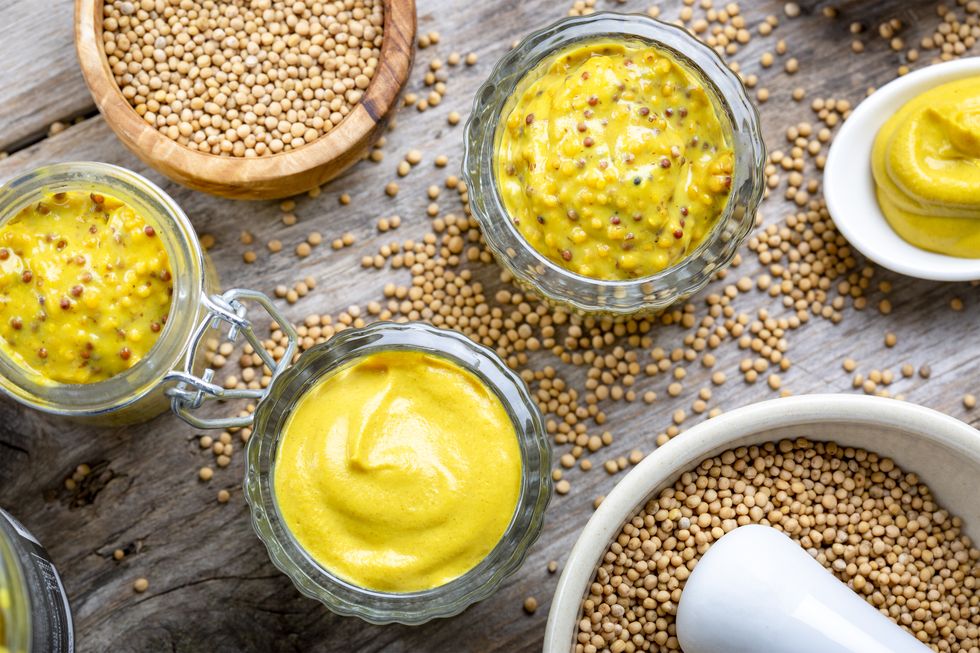 different types of mustard and mustard seeds on a rustic wooden board