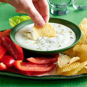 a bowl of dip with sliced veggies and potato chips on a platter