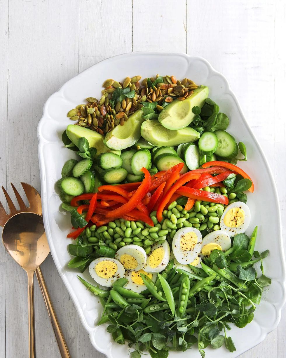 green machine power salad on a white serving dish with gold utensils on a white wooden surface