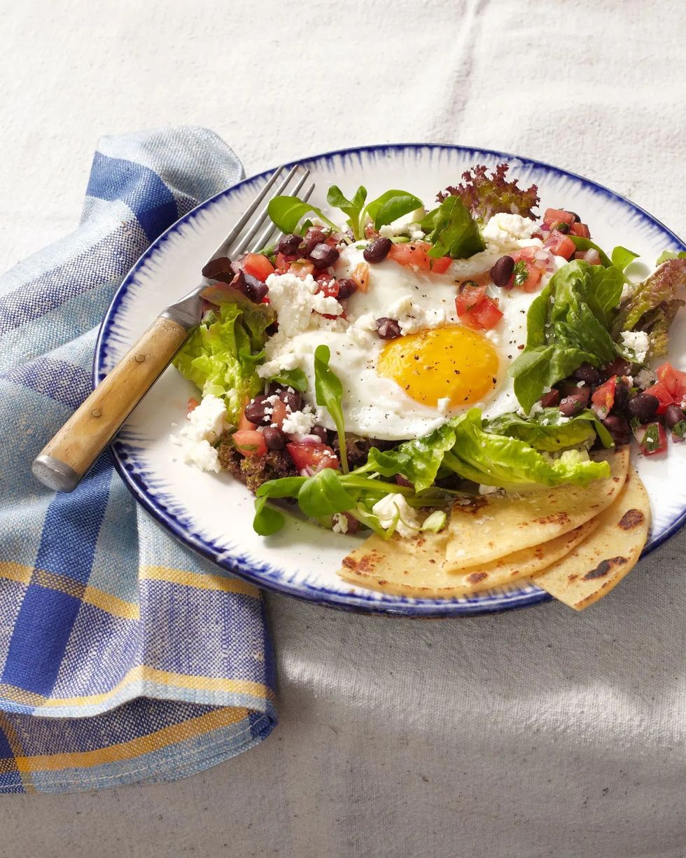 huevos rancheros salad with a fried egg on top with a blue plaid napkin on a white table cloth