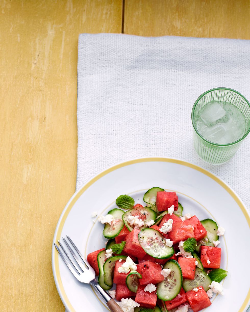 watermelon cucumber salad on a white plate with a wooden fork on a white cloth on a yellow background