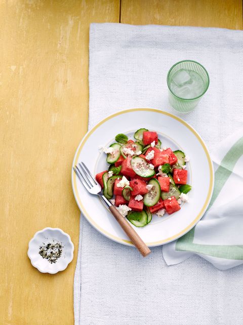 watermelon cucumber salad on a white plate with a wooden fork on a white cloth on a yellow background