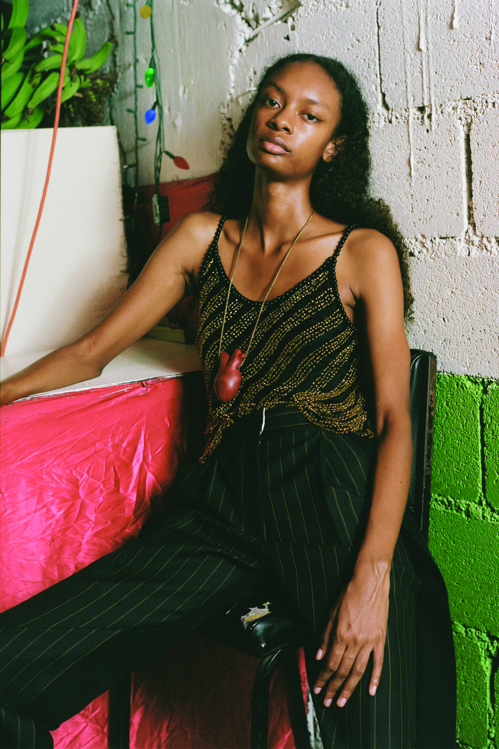 a model wears a beaded camisole and tailored pants with a heart pendant