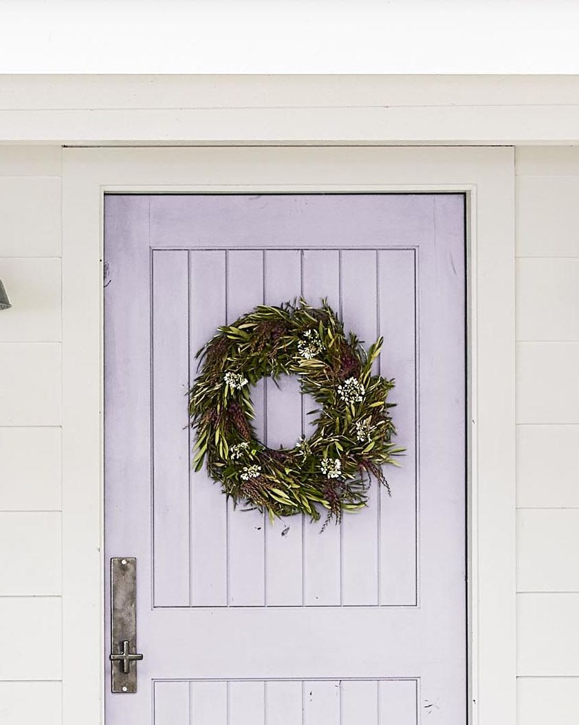 an olive branch wreath hung on a lavender painted door