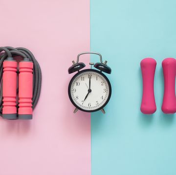 directly above shot of alarm clock with jump rope and dumbbells on colored background