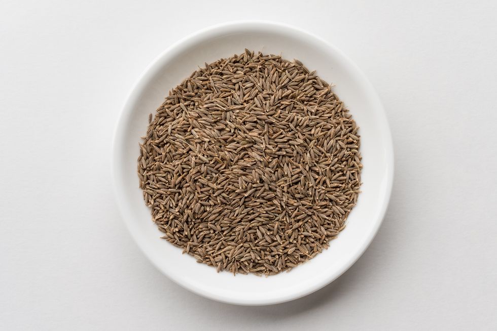 directly above shot of cumin seeds in plate over white background