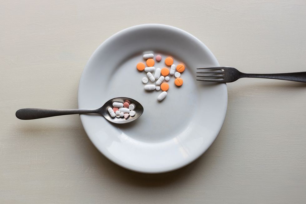 directly above shot of pills in plate by fork and spoon against wooden table