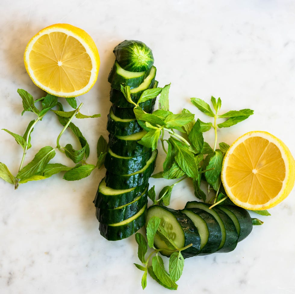 directly above shot of sliced cucumber and lemon with mint on white marble