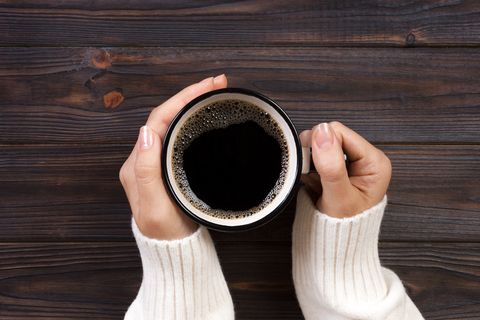 directly above shot of woman hands holding black coffee in cup on table