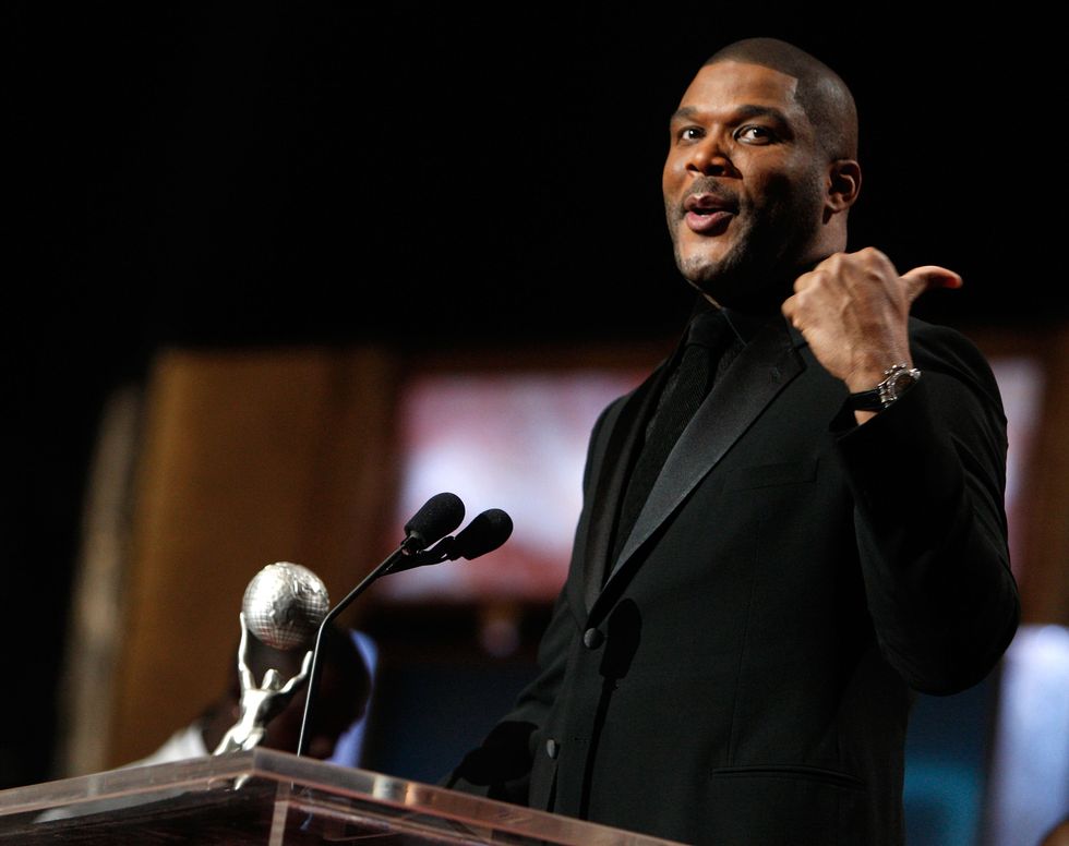 man pointing behind his back as he speaks at a podium with a trophy on it