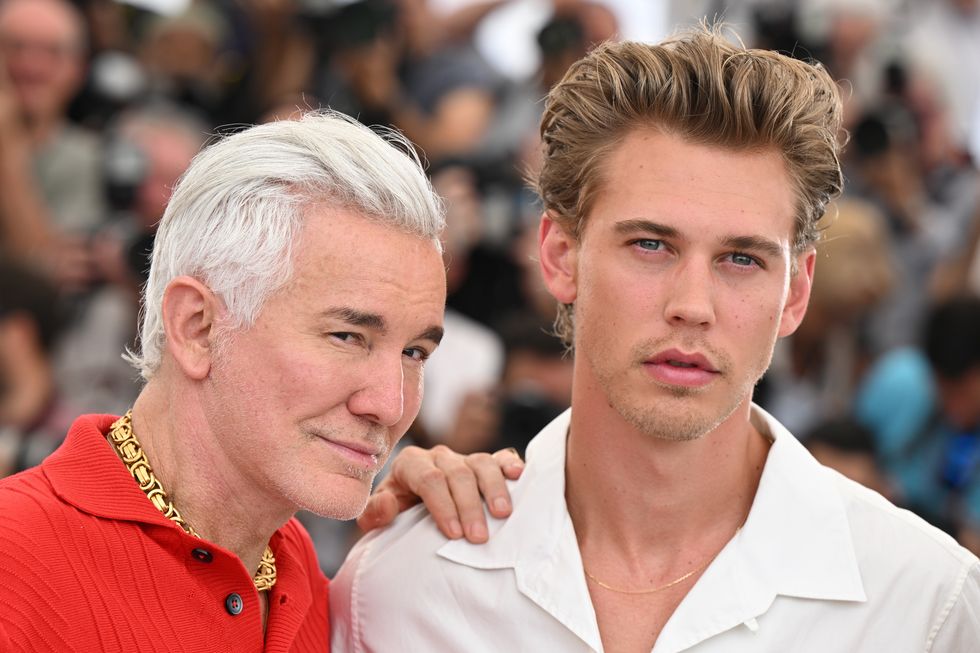 baz luhrmann, wearing a red shit and gold necklace, with his hand on the shoulder of austin butler, who is wearing a white shirt and looking directly into the camera