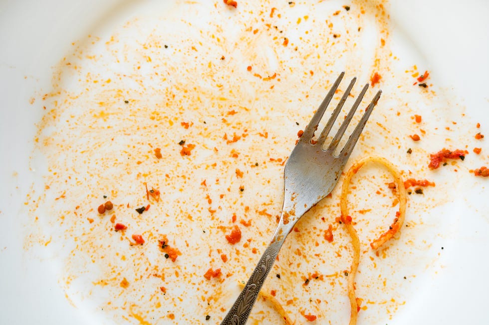 a dirty empty plate of pasta or spaghetti, a fork on a wooden table used cutlery, symbolize the end of lunch or dinner