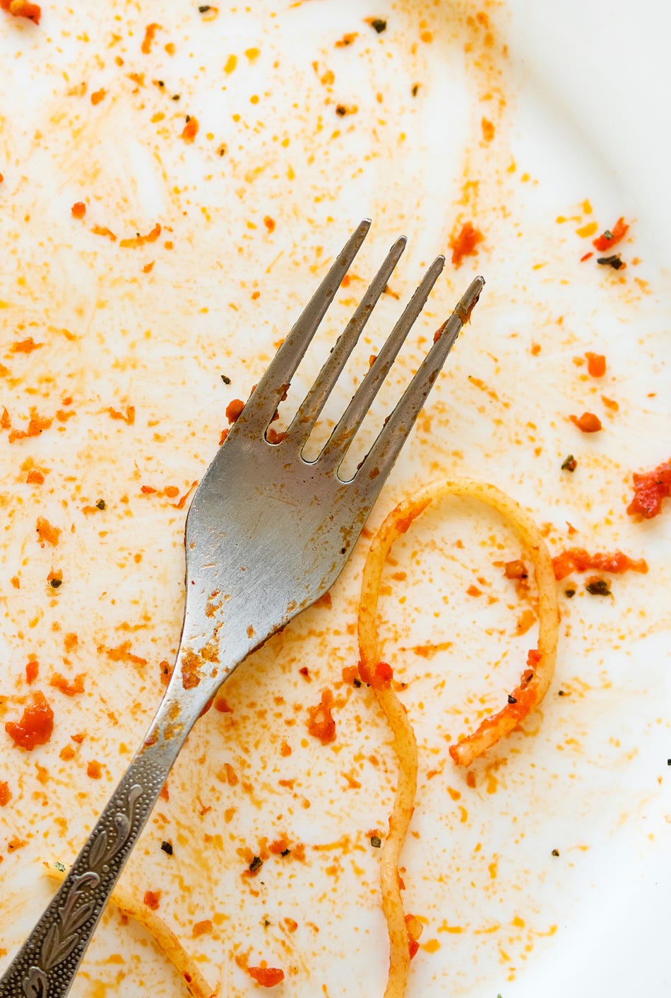 A dirty empty plate of pasta or spaghetti, a fork on a wooden table. Used cutlery, symbolize the end of lunch or dinner. a dirty empty plate of pasta or spaghetti, a fork on a wooden table used cutlery, symbolize the end of lunch or dinner