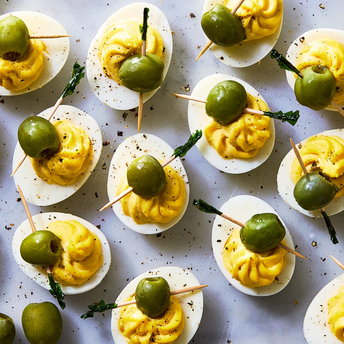deviled eggs decorated to look like dirty martinis with olives on a toothpick