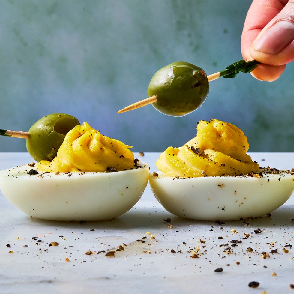 deviled eggs decorated to look like dirty martinis with olives on a toothpick
