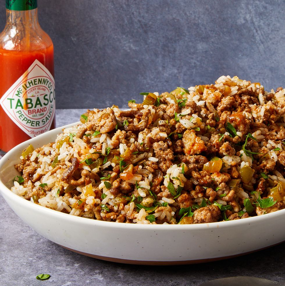dirty rice topped with chopped parsley in a white bowl next to a bottle of hot sauce