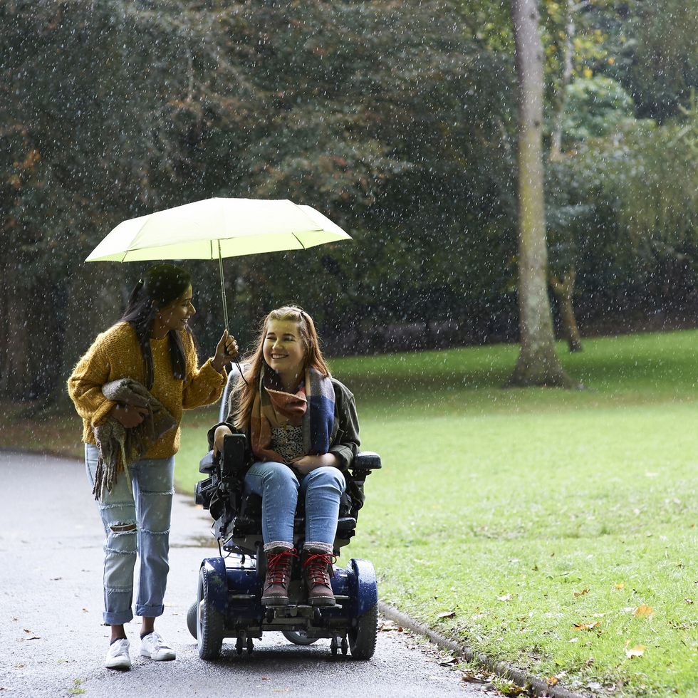 disabled woman and friend under umbrella in autumn park