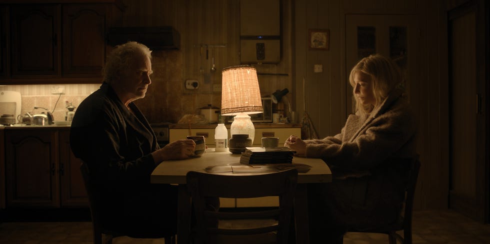 Two people sit at a table in a dimly lit kitchen and talk