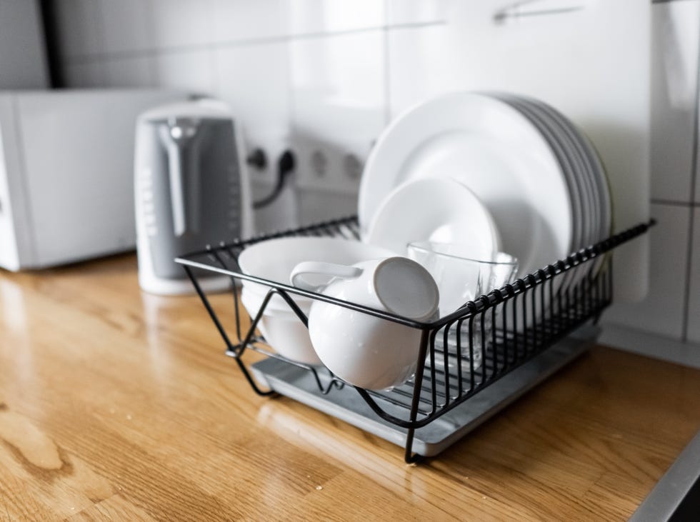 dish rack holds many dishes and cups against wooden countertop, white wall tiles, sink and faucet budget and lightweight antimicrobial dish drainer with drain board at modern scandinavian kitchen