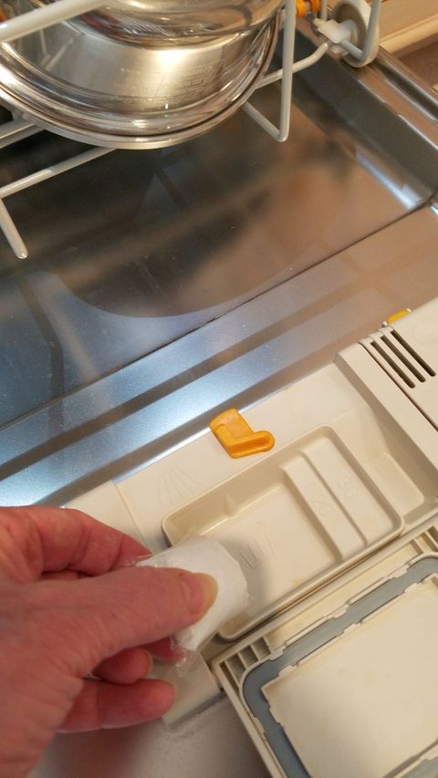 a hand placing a dishwasher detergent pod into the soap dispenser of a dishwasher