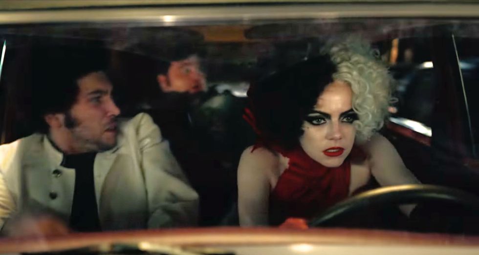 emma stone in a red dress behind the wheel of a car as she drives angrily in disney's cruella