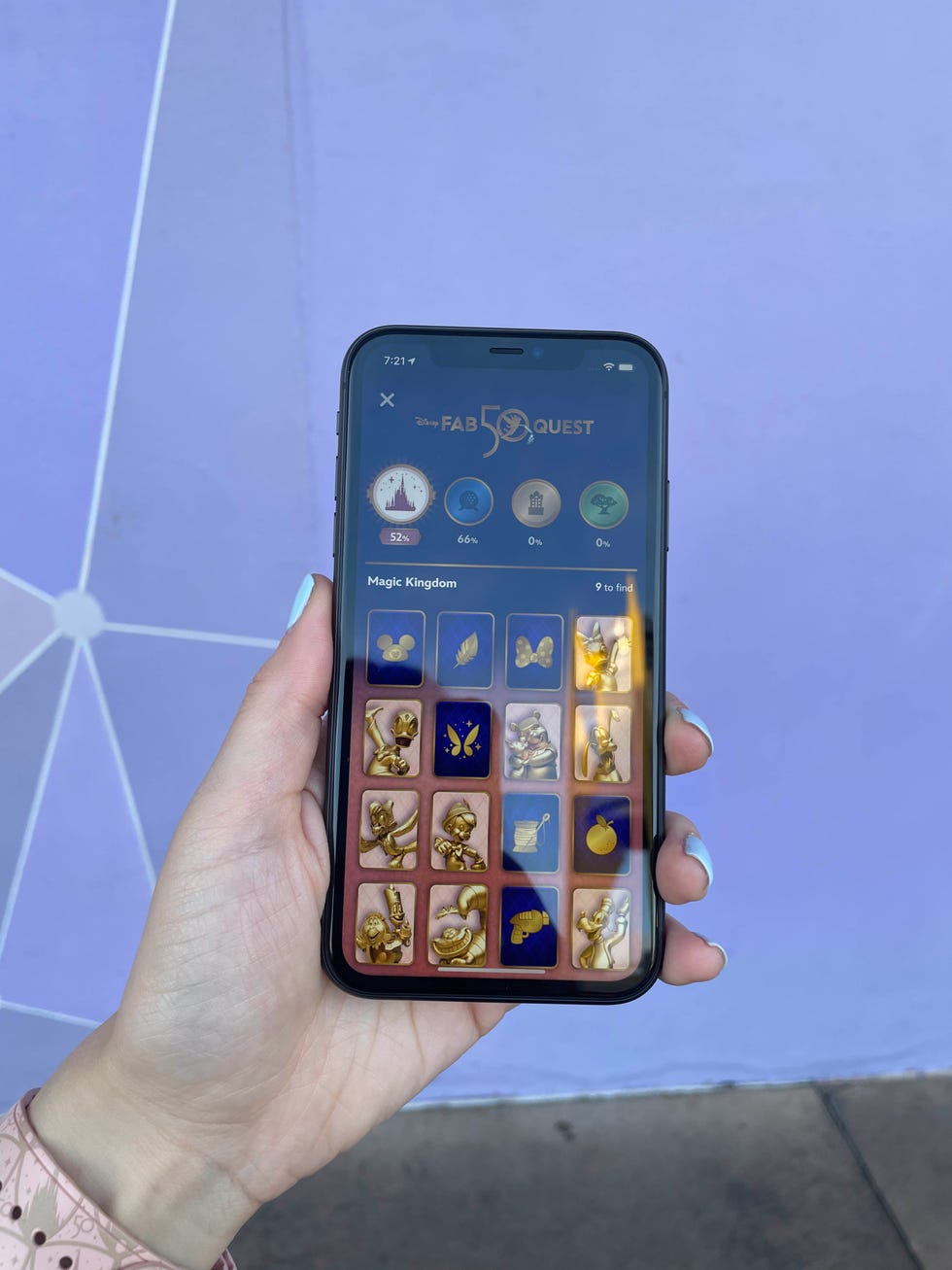 a cell phone screen showing an app with disney gold character fab 50 quest against a purple wall at walt disney world magic kingdom park