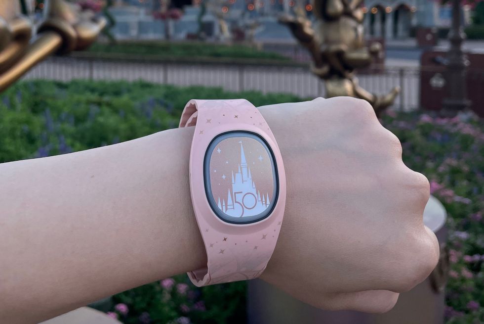 a pink and gold magicband plus on a wrist with magic kingdom park in the background