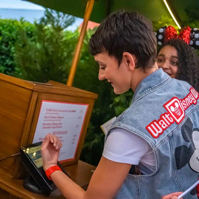 a person wearing a magicband plus at walt disney world making a payment by taping their wristband to a countertop payment kiosk