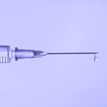 disposable sterile syringe with drop of fluid medication on thin needle on violet background macro photography with copy space demonstrating very peri color of 2022 year