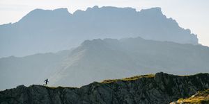 Distant trail runner traverses mountain landscape