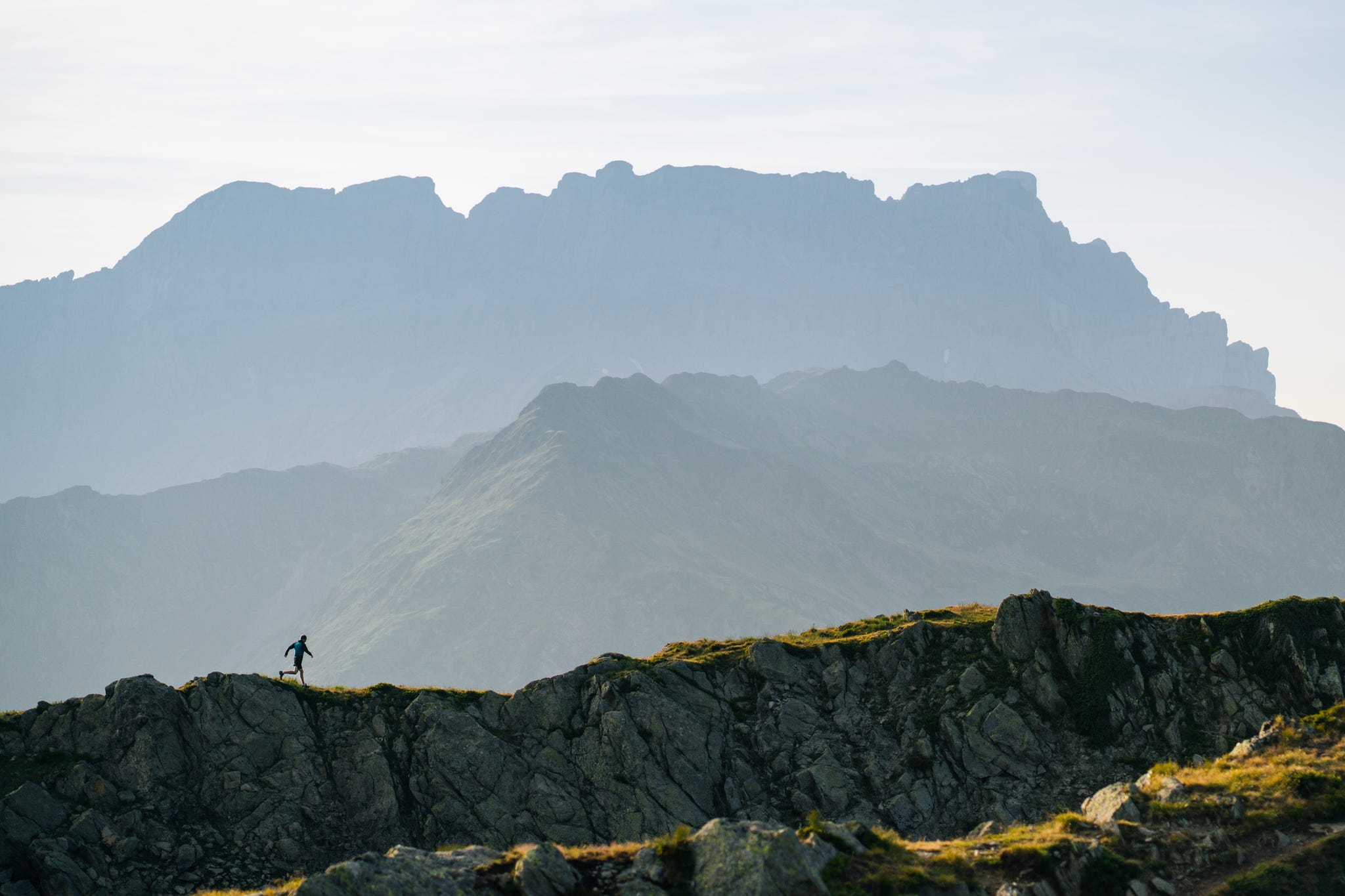 Distant trail runner traverses mountain landscape