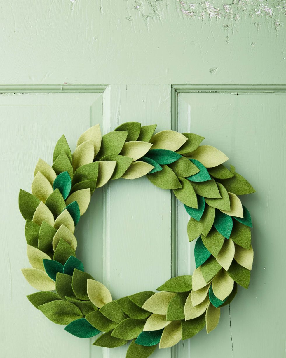 wreath made from different shades of green felt that have been cut into leaf shapes hung on a green door