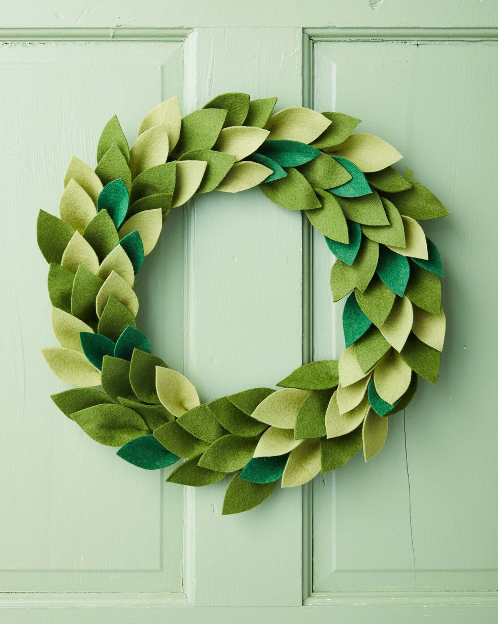 wreath made from different shades of green felt that have been cut into leaf shapes hung on a green door