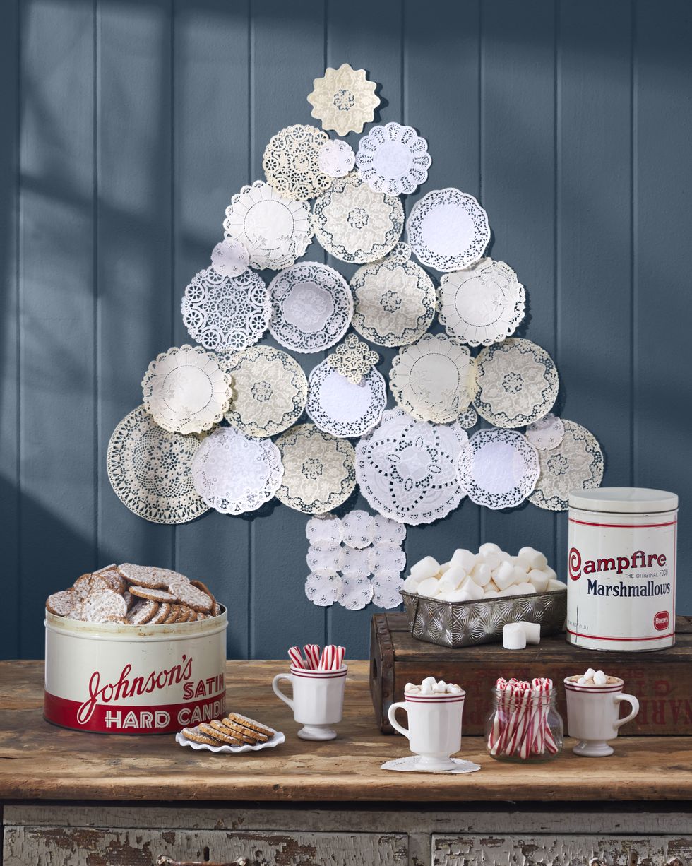 paper doilies hung in the shape of a tree on a blue wall above a hot chocolate buffet