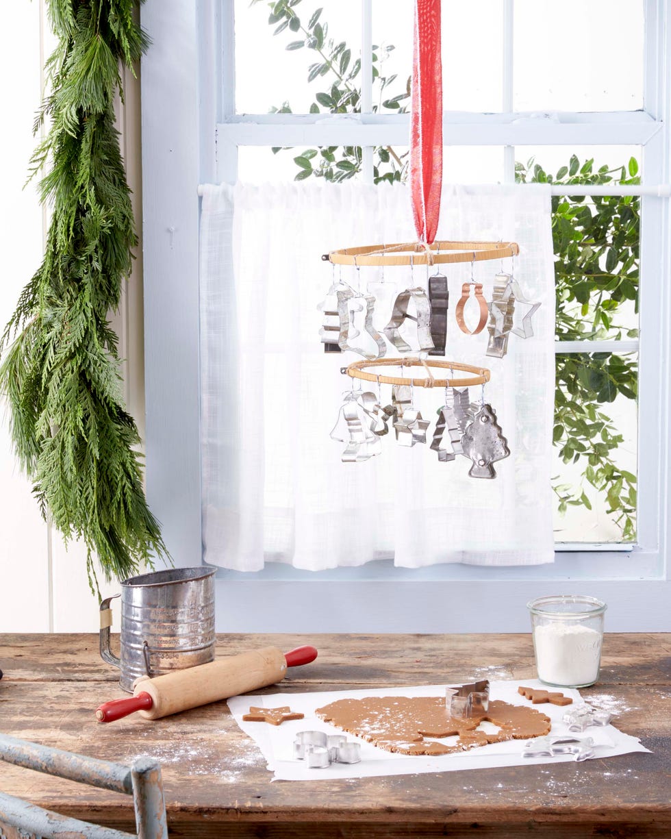 a hanging mobile made from embroidery hoops and vintage cookie cutters hung above a table where gingerbread cookies are being made