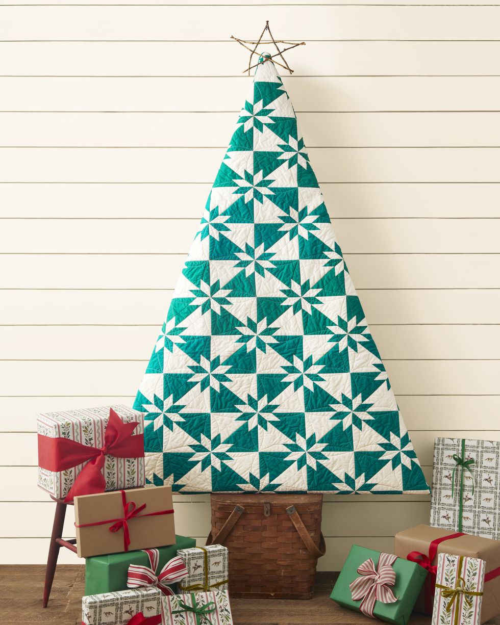 a green and white quilt shaped like a christmas tree set on a wooden picnic basket with presents around the base