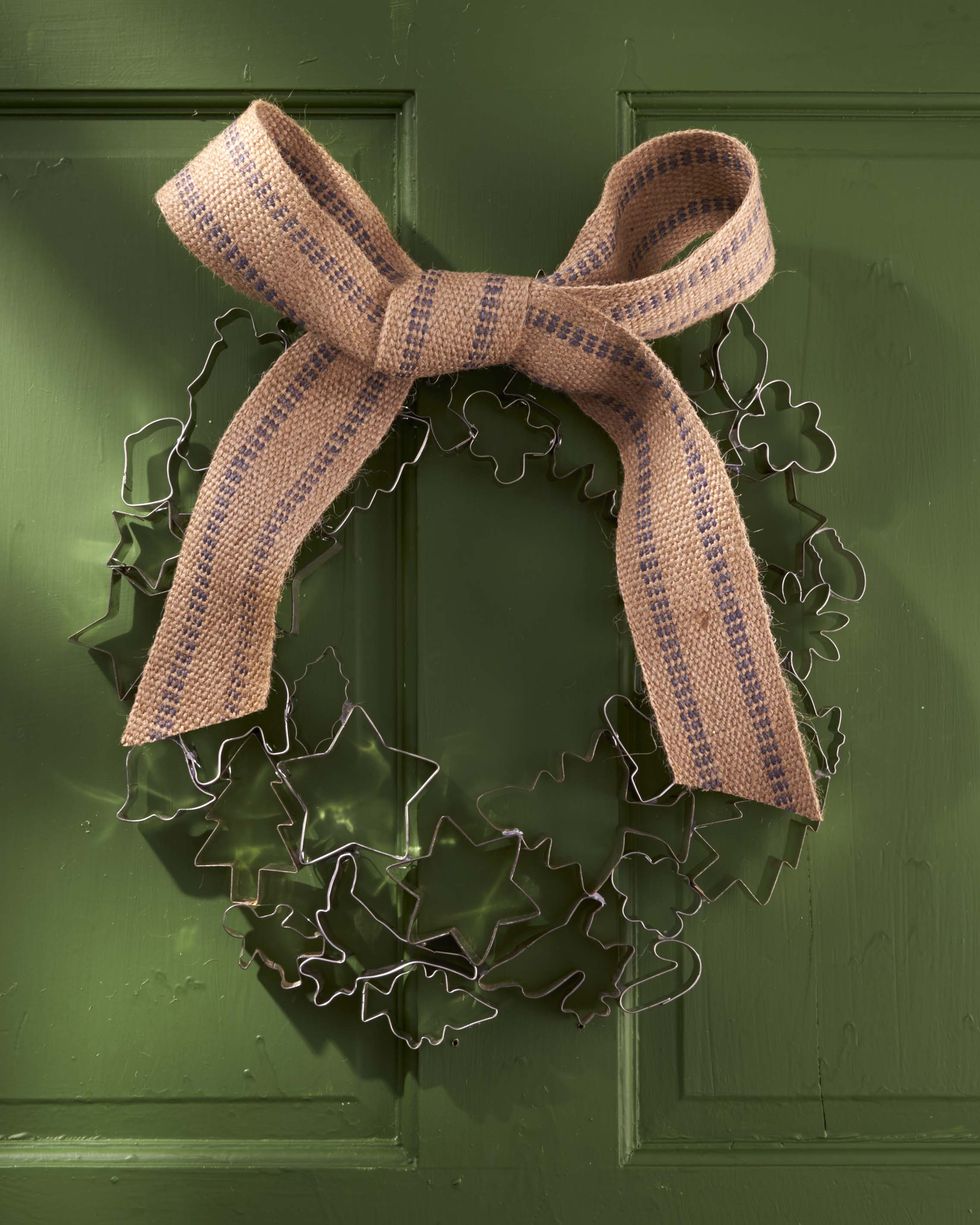a round wreath made from vintage cookie cutters adorned with a jute bow and hung on a green door