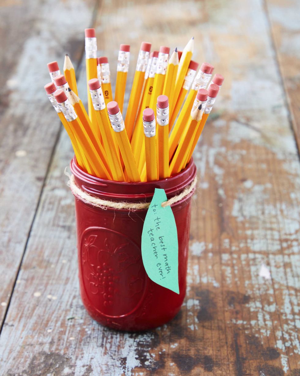 a mason jar painted red with a green leaf gift tag and pencils in the gar