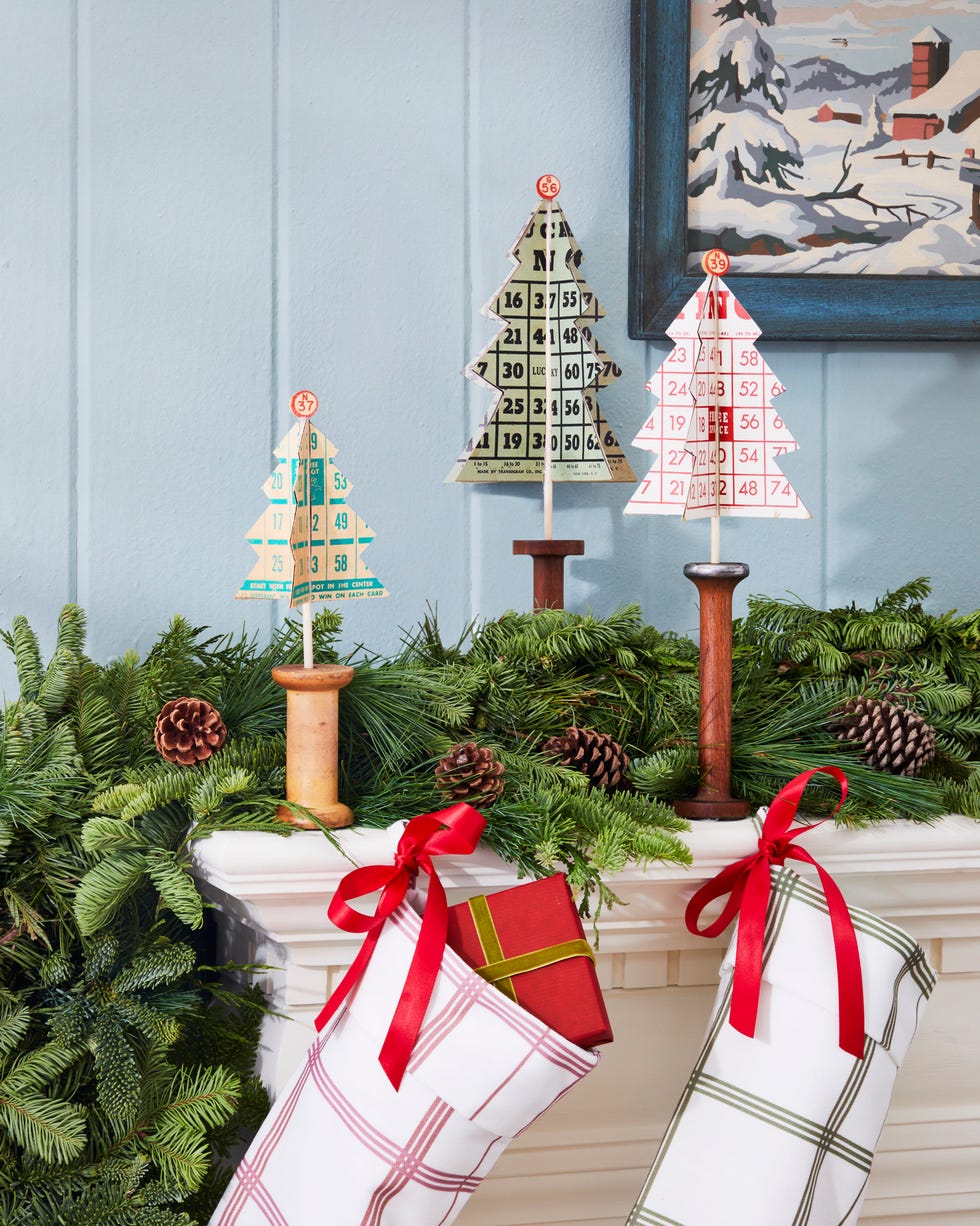 christmas trees made from vintage bingo cards set in antique wooden spools all displayed on a decorated mantel