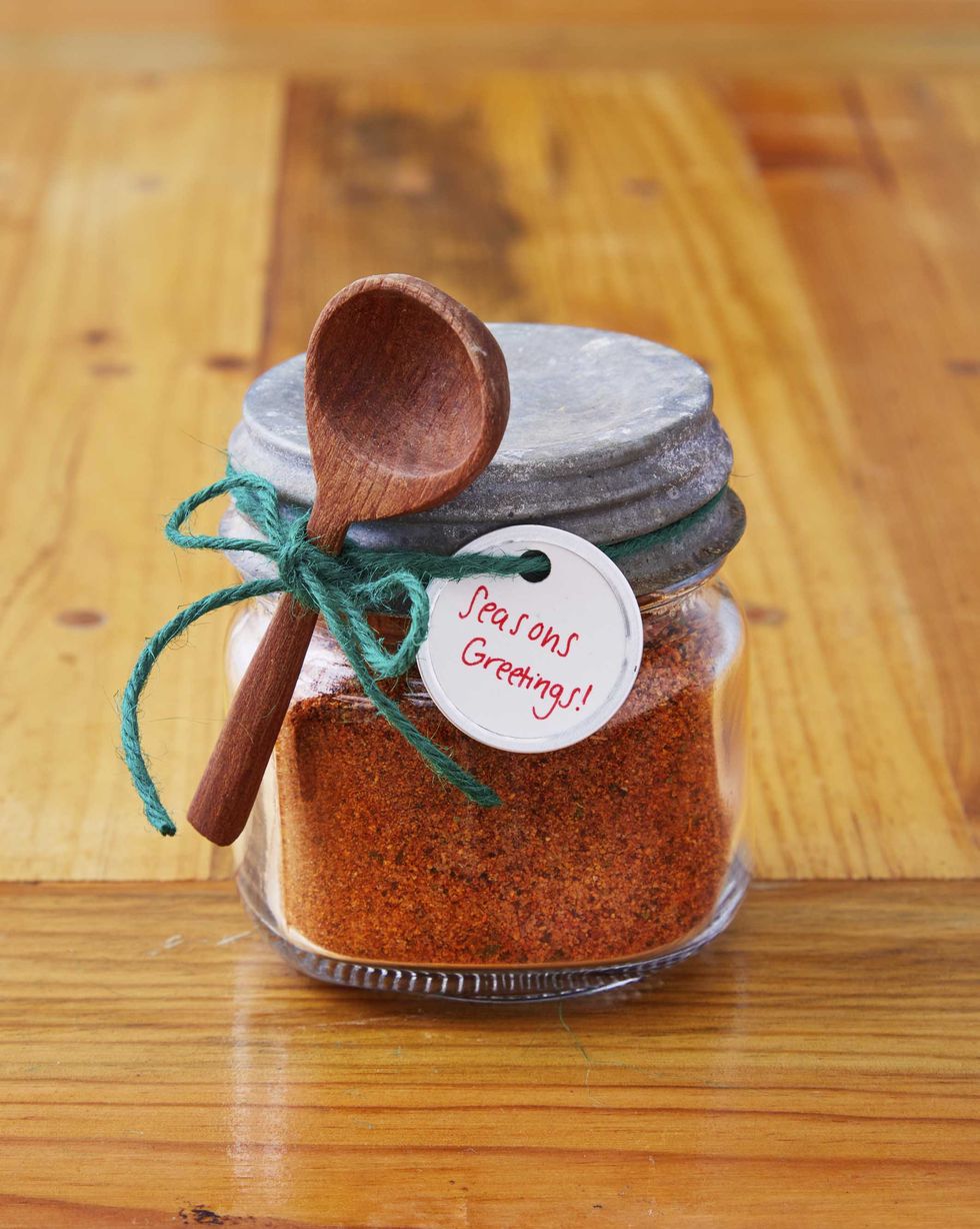 A small mason jar filled with spice mix, a small wooden spoon, and a gift tag attached to the outside with green twine