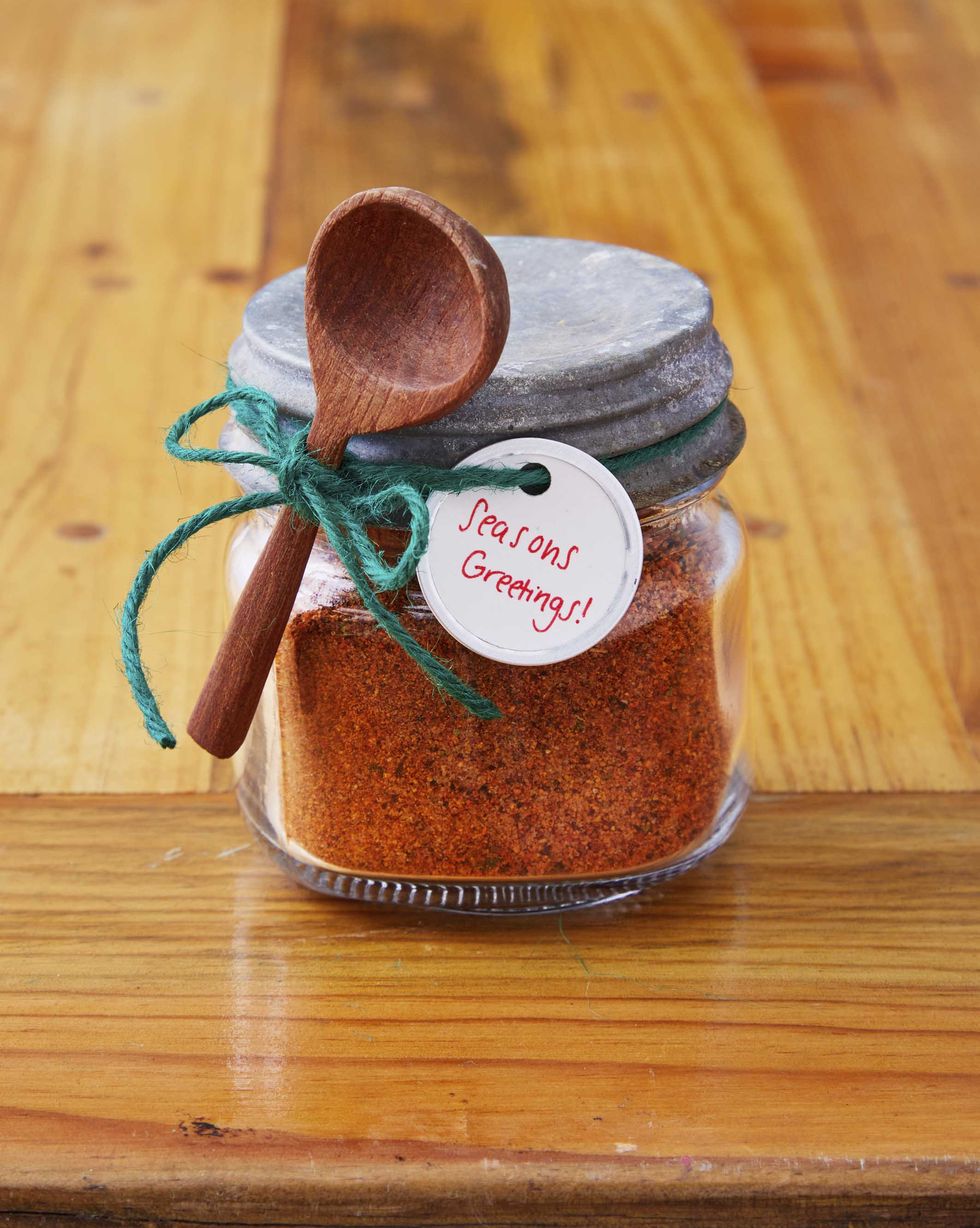 small mason jar filled with spice mix with a small wooden spoon and gift tag attached to the outside with green twinewith
