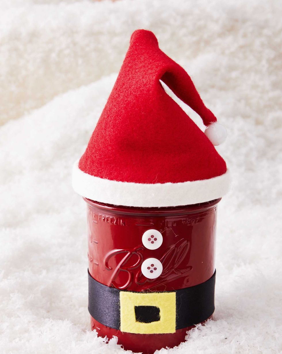 A mason jar decorated to look like a Santa costume with a hat made of red felt and a belt made of black ribbon and yellow felt