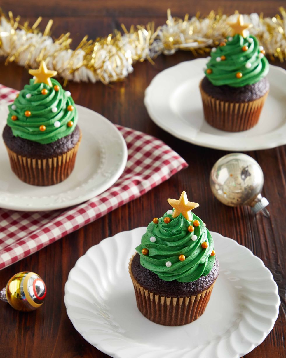 Chocolate cupcakes decorated with green frosting that looks like a tree and small gold and white candy ornaments