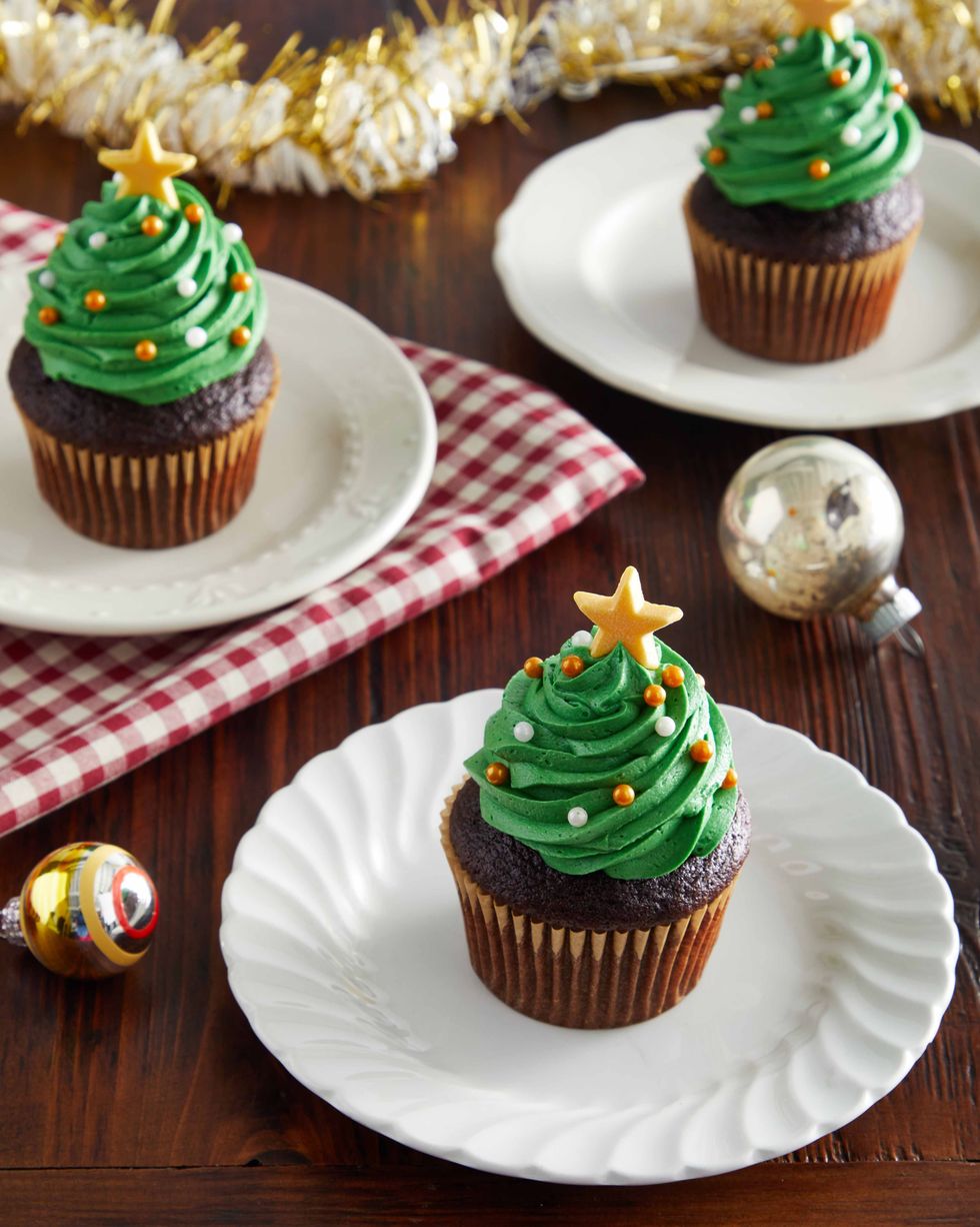 chocolate cupcakes decorated with green frosting made to look like a tree and small gold and white candy ornaments