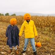 DIY Couples Costume - Jack o Lantern Couple in Pumpkin Patch costumed couple walking in pumpkin patch wearing diy jack o lantern heads, raincoats, and jeans