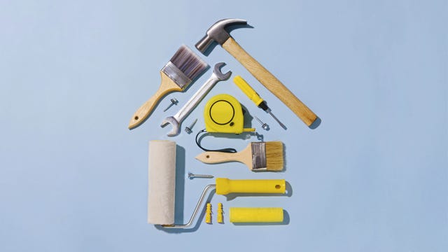 creative flat lay still life with an assortment of household tools forming a small house in a diy, renovations, construction or maintenance concept over blue