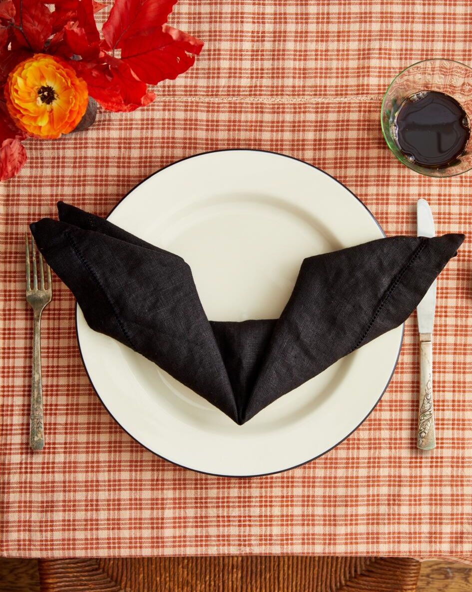 black linen napkin folded into the shape of a bat on a set table with an orange patterend table cloth